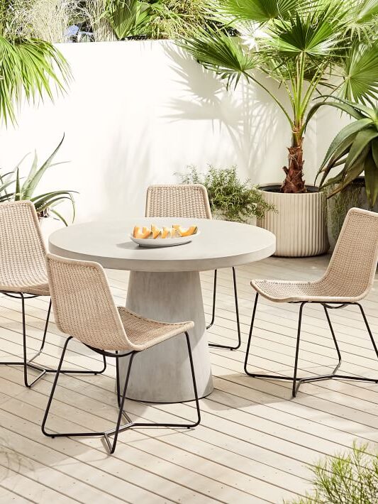 A concrete round pedestal table with woven and metal outdoor chairs