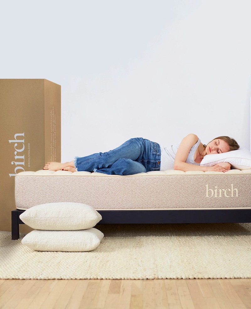 A young woman. sleeps on her side on top of a Birch Mattress while the box for the mattress sits upright behind her