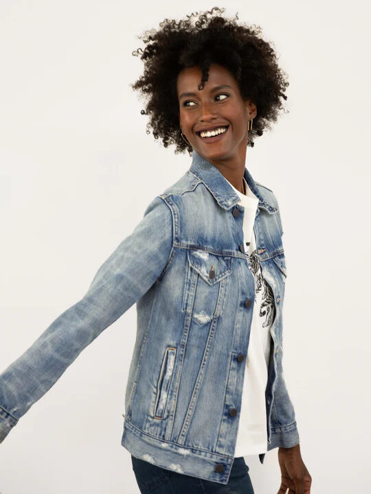 Model wearing Able Clothing distressed denim jacket while smiling and looking back