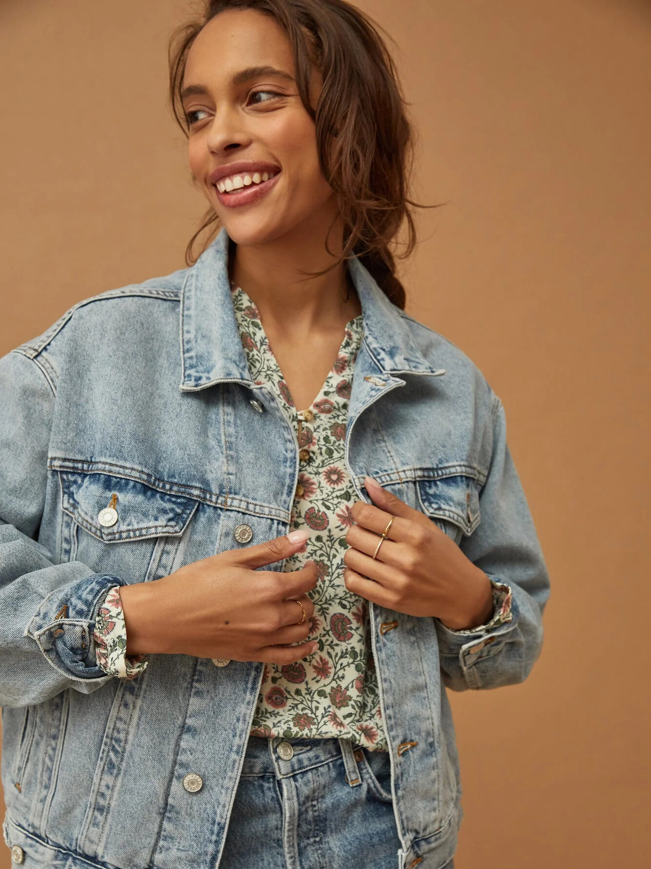 Model wearing AGOLDE Organic Cotton Denim Jacket with a floral shirt underneath and smiling behind them
