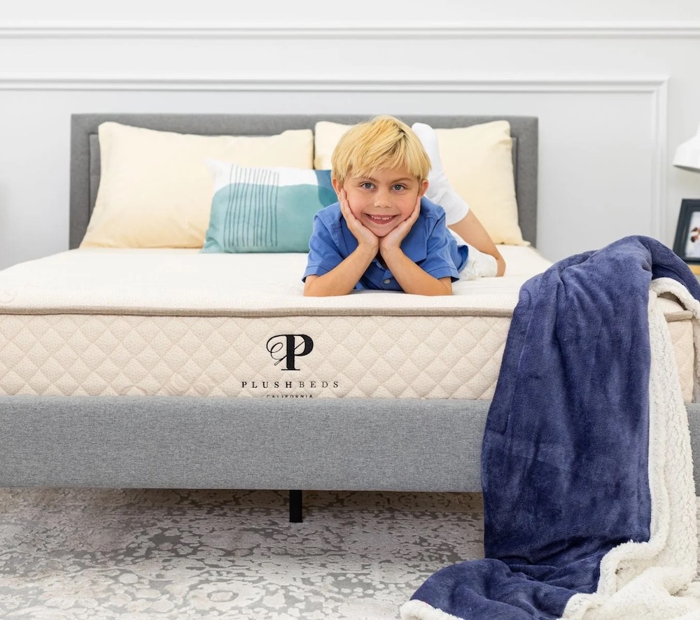 A young boy lays with his head in his hands and smiles on top of a Plushbeds full size mattress.