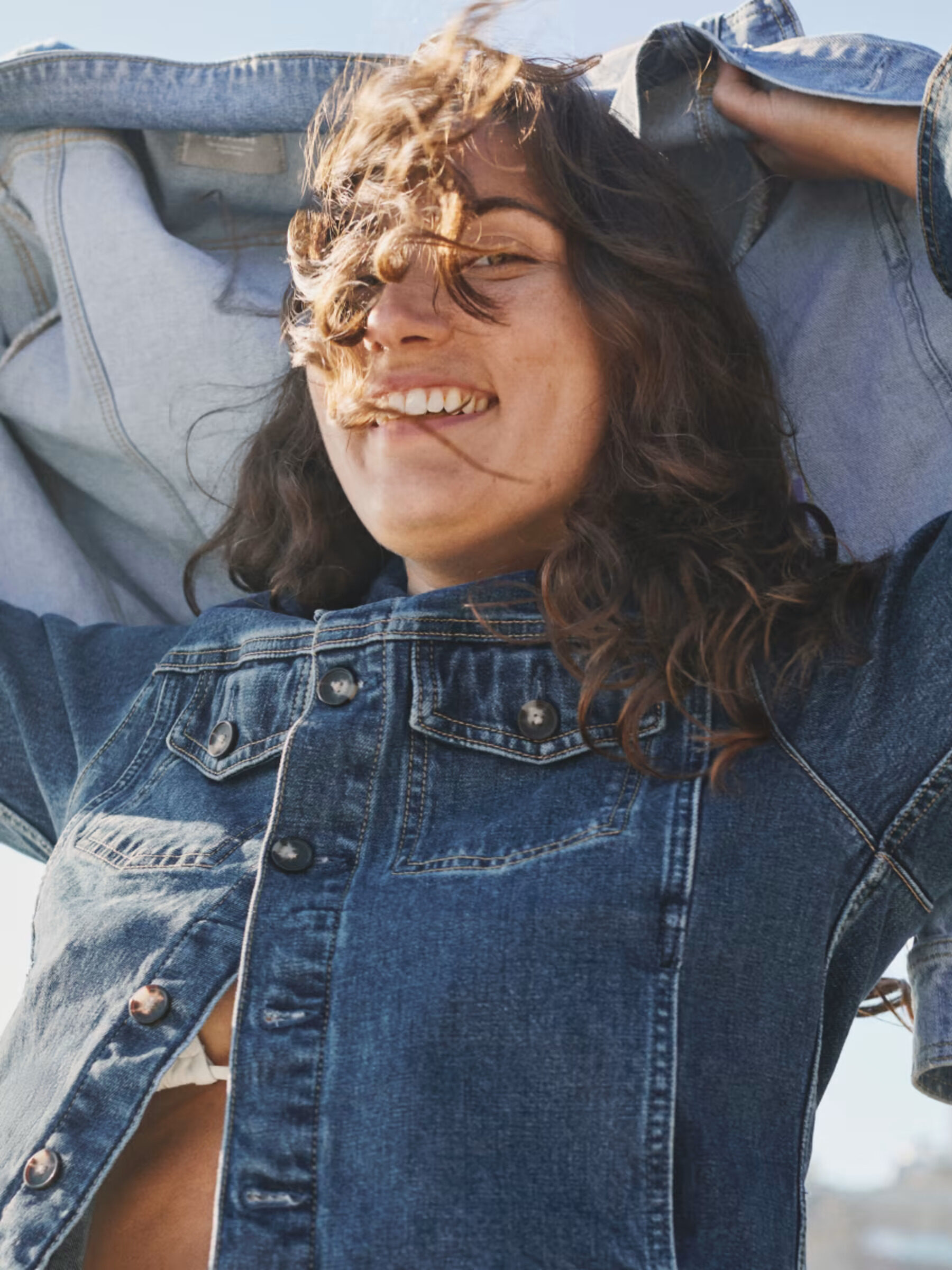 Model wearing an Everlane Dark Wash Jean Jacket while smiling and the wind blowing through their hair