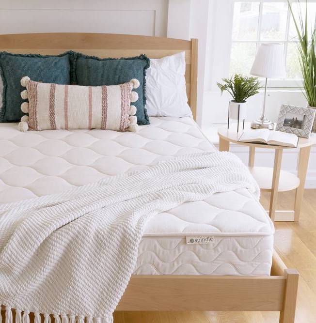 A bare mattress with a blanket across it, the spindle mattress logo is visible on a tag by the foot of the bed