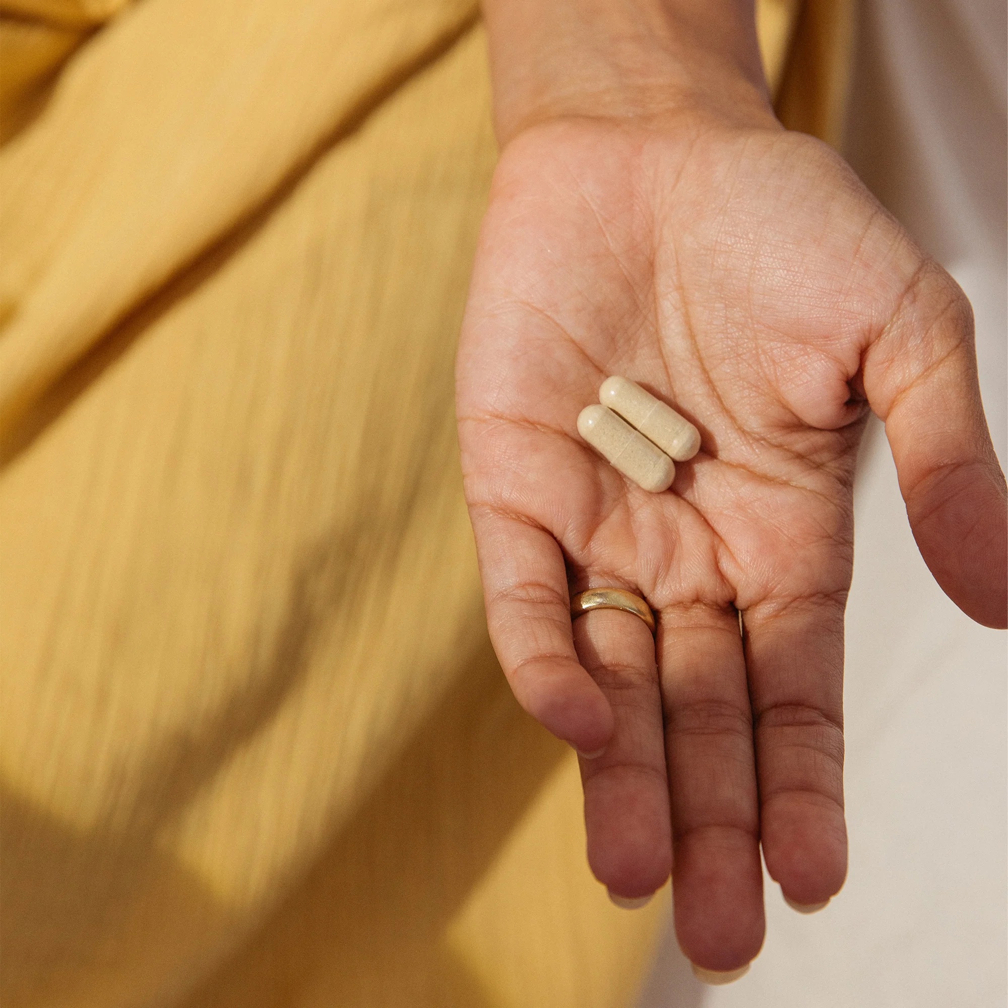 A hand holding 2 capsules of Needed. 