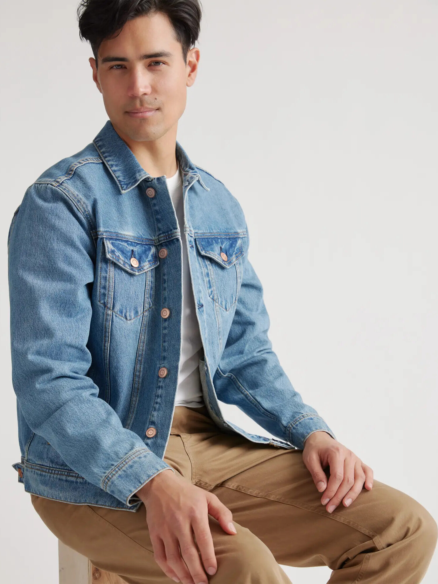 Model wearing a Quince Organic Cotton Denim Jacket while seated on a chair