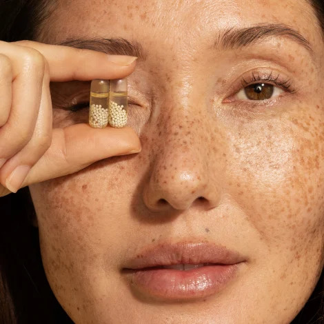 A model holding up two Ritual multivitamin capsules with omega 3 over their eye.