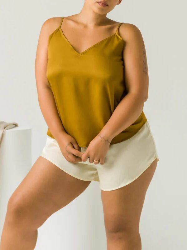 Only the torso and legs of a model wearing an ochre colored silk cami and cream silk sleep shorts are visible