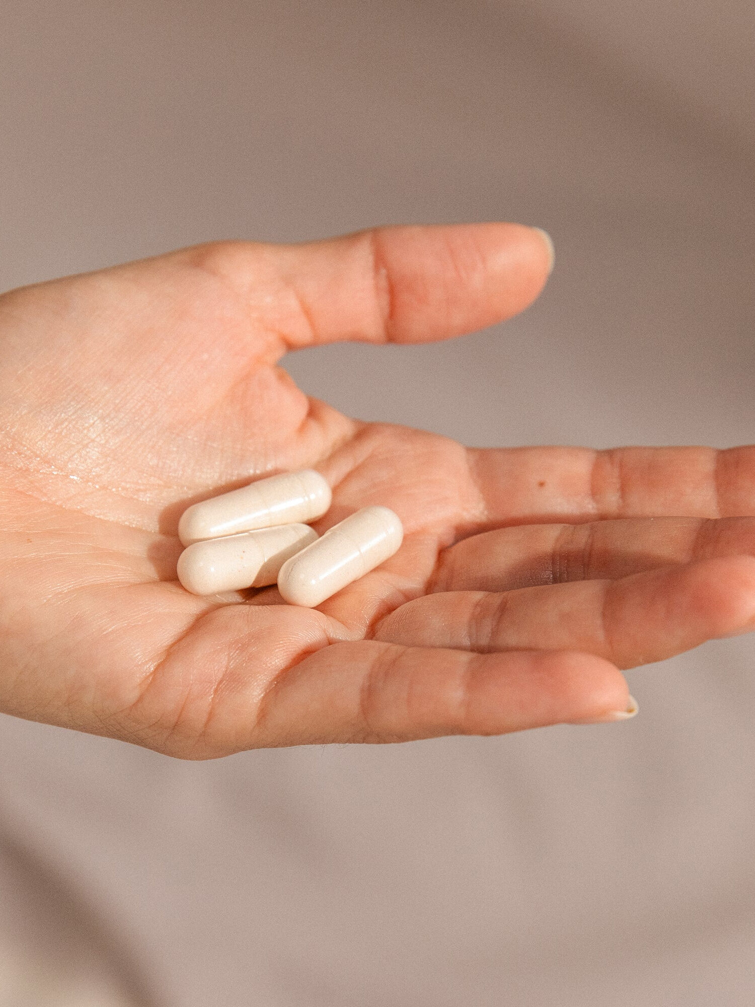 A hand holding three Needed Multivitamin capsules.