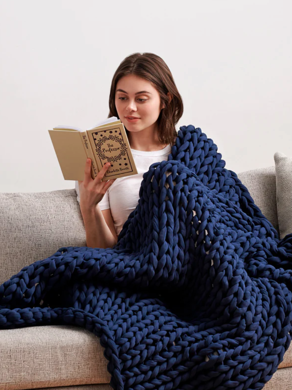 A woman reads a book with a blue blanket draped over her