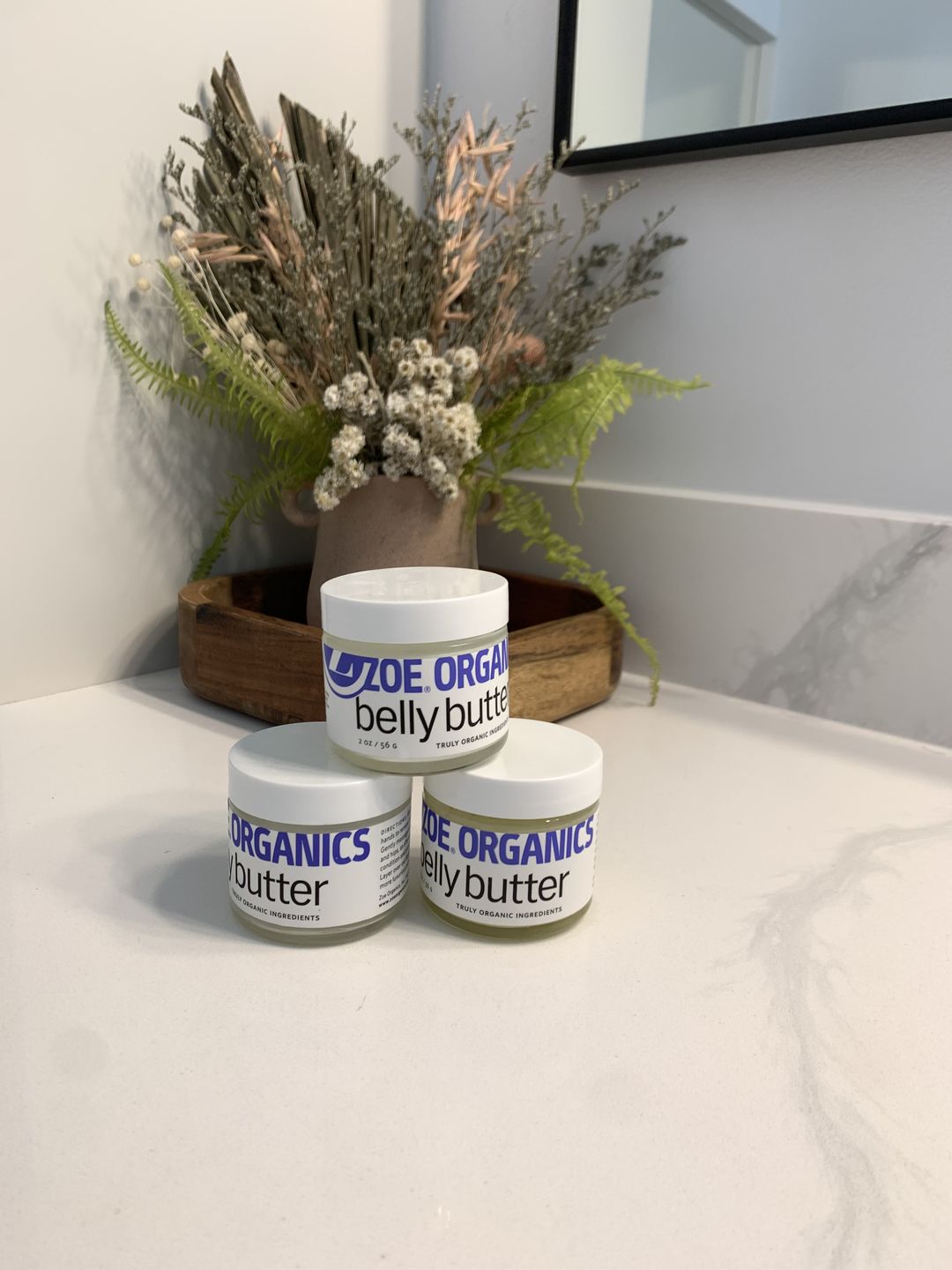 A stack of belly butter jars in front of a plant. 