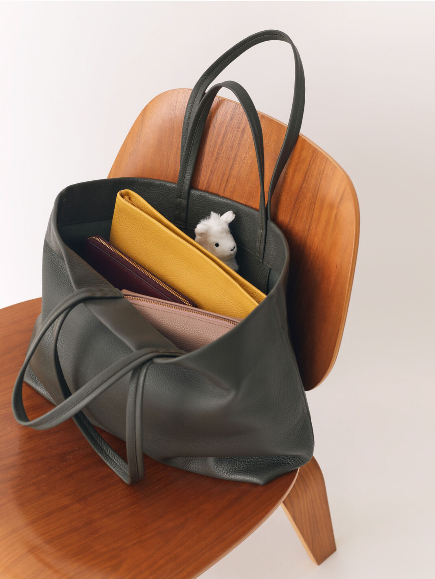 A green bag sits open on a chair, showing the contents withint (two pouches, a folder, and a stuffed animal)