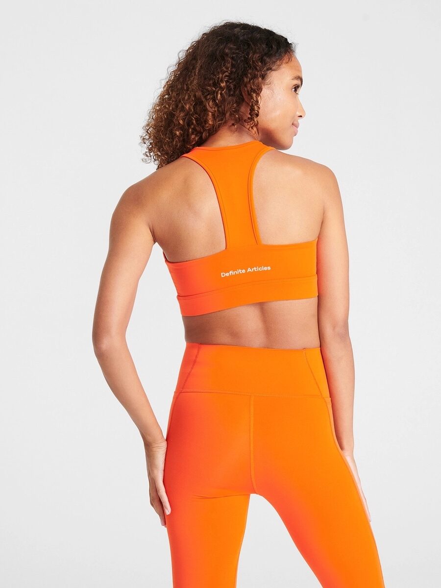 Model facing away from the camera, wearing orange sports bra and matching leggings