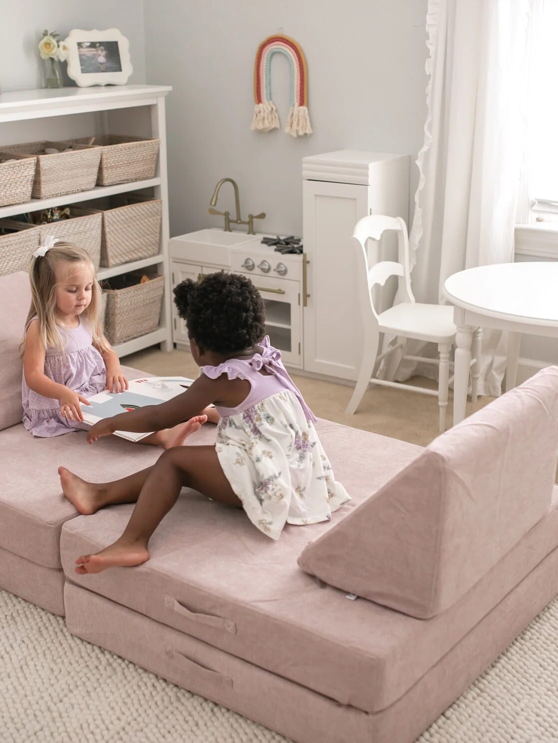Two girls play on a light pink play couch shaped into a sofa