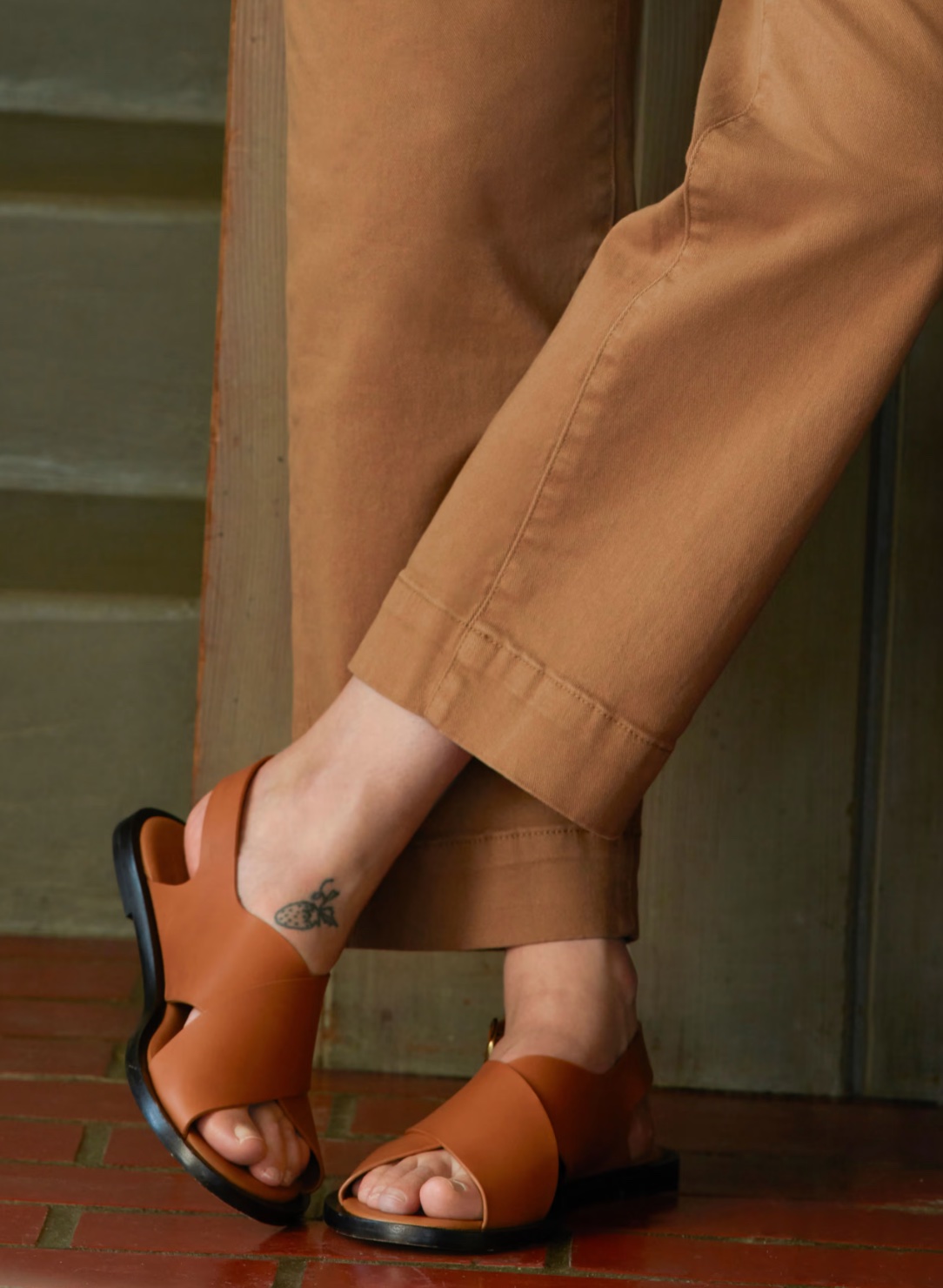 A model's legs are crossed at the ankle, showing off Everlane leather sandals.
