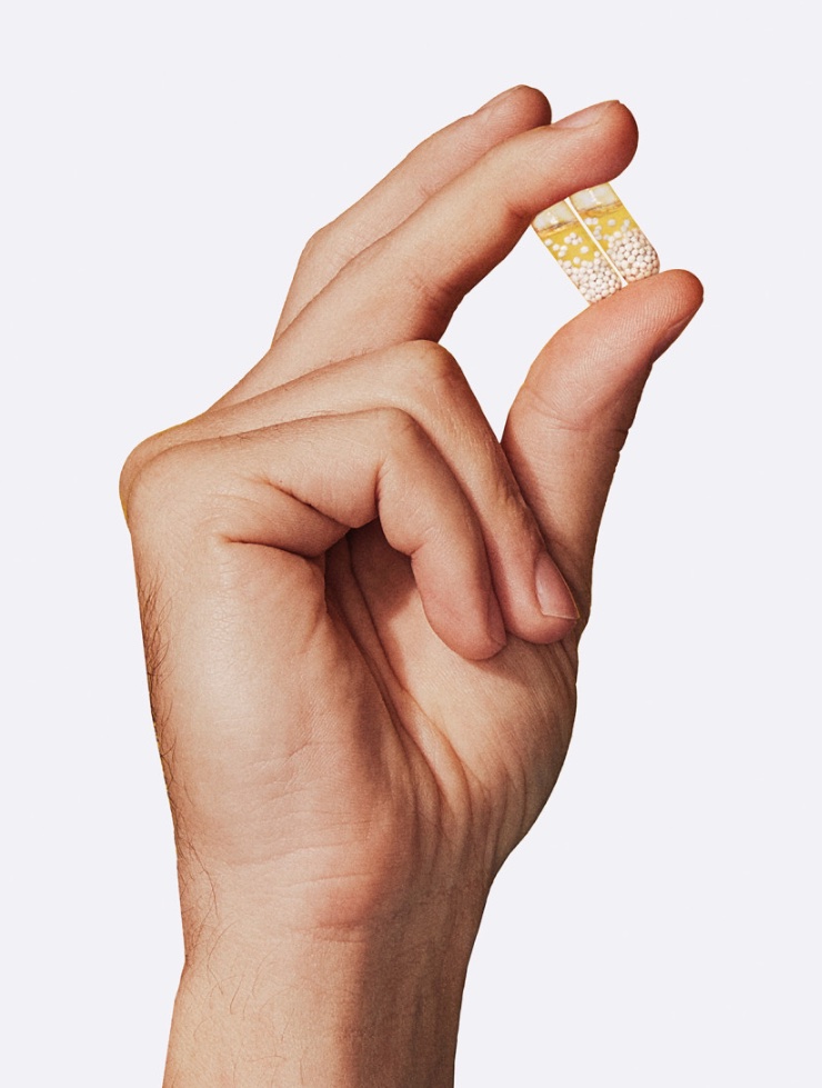 A close up of a hand holding two multivitamin capsules.