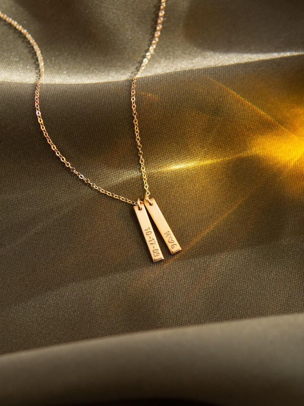GLDN bar necklace lays on olive green fabric.