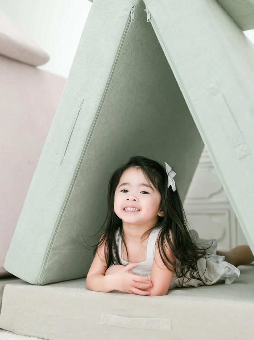 A girl lies under a propped up mint green play cushion