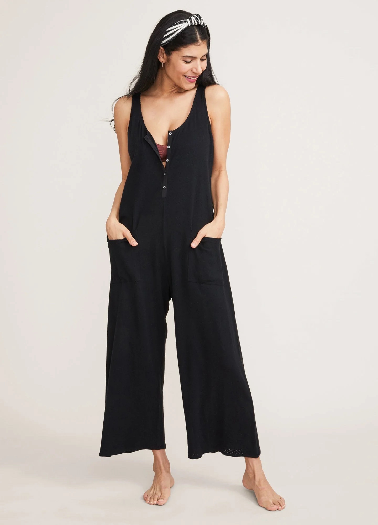 A model has her hands in the pockets of a black nursing jumpsuit.