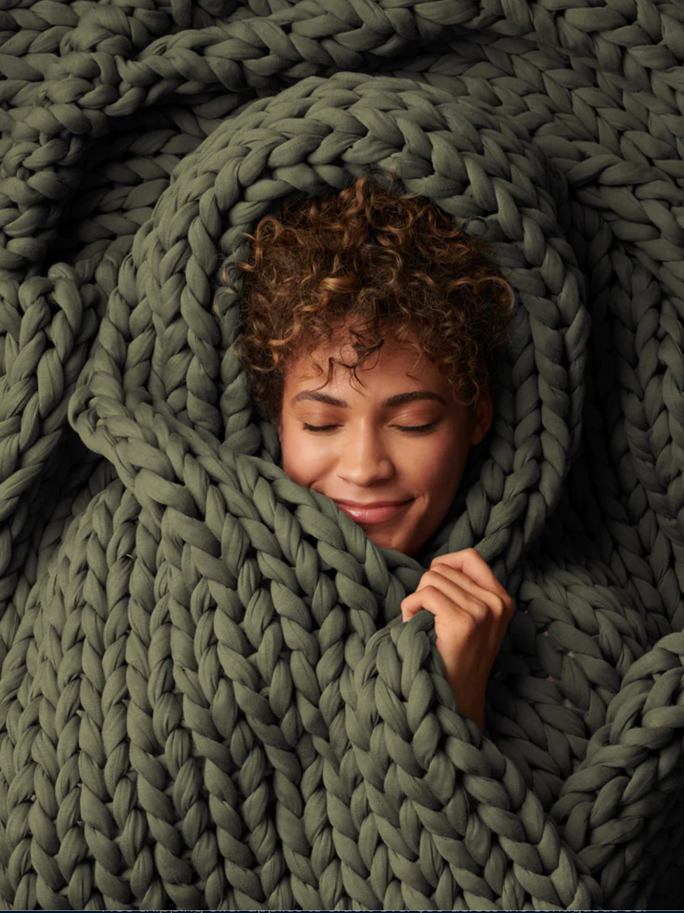 A woman lies down with her eyes closed all wrapped up in a green blanket