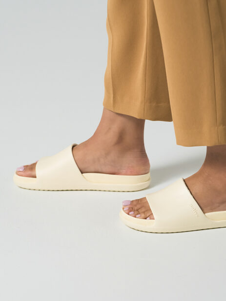 A pair of cream slide sandals on a model's feet.