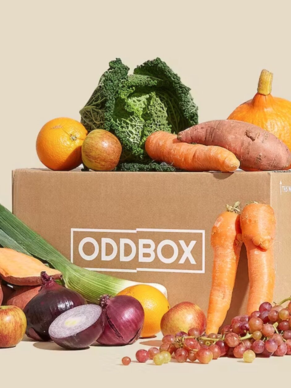 An Oddbox with vegetabels and grapes sitting on and around it.