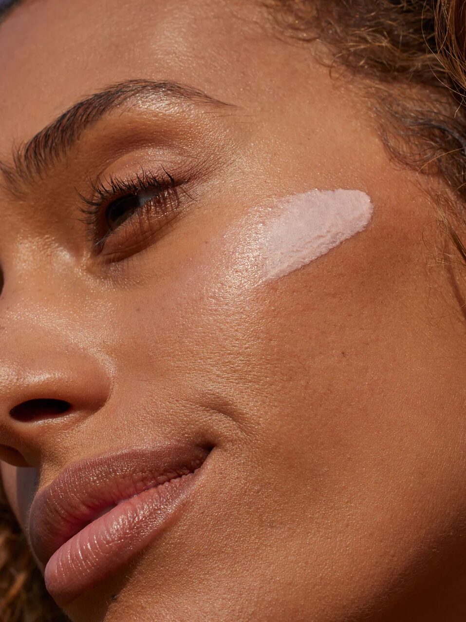 A model looks serenely away from the camera and a swipe of sunscreen lays on her cheekbone.