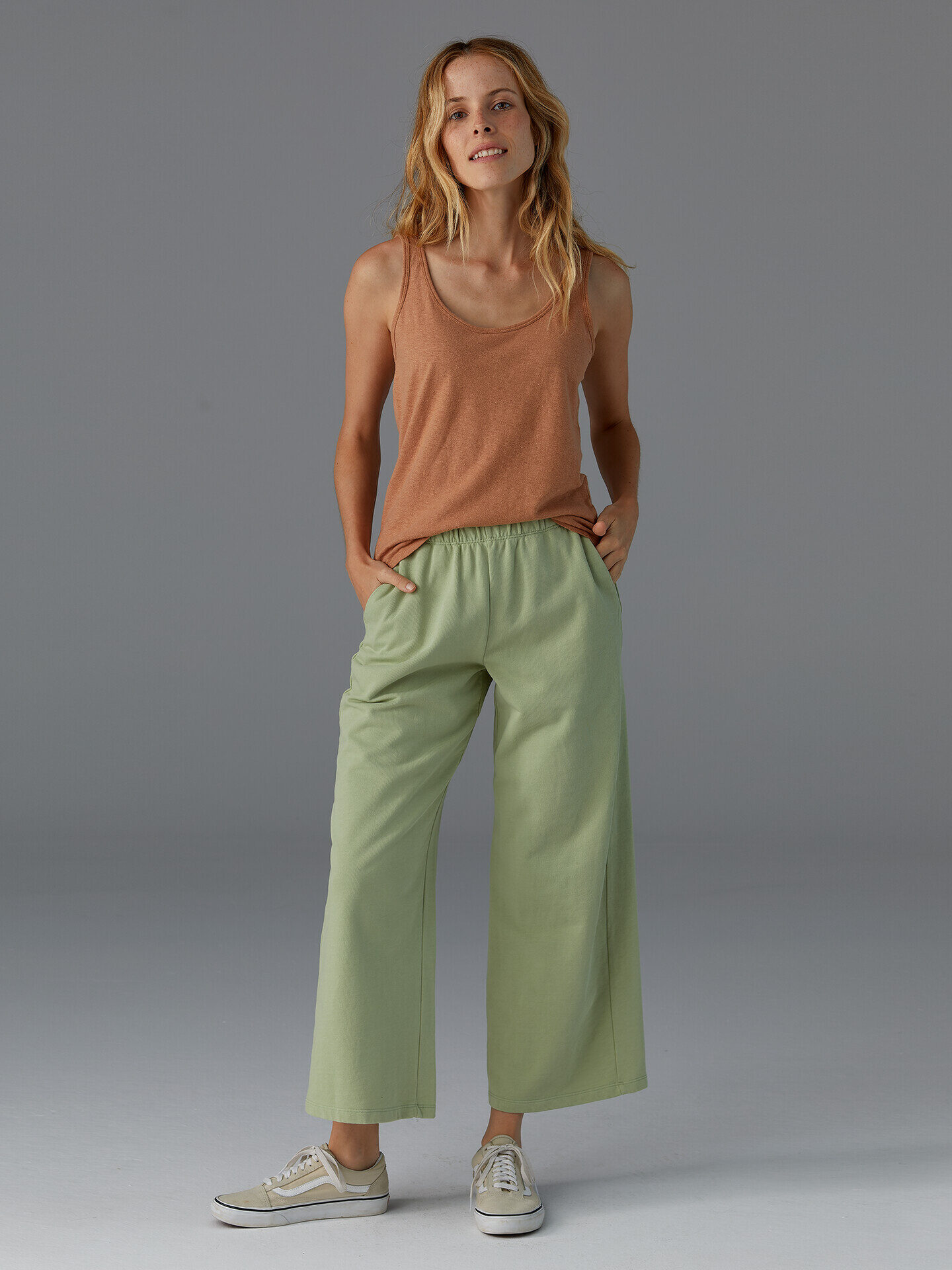 Model in brown tank and sage green wide leg pants and tennis shoes