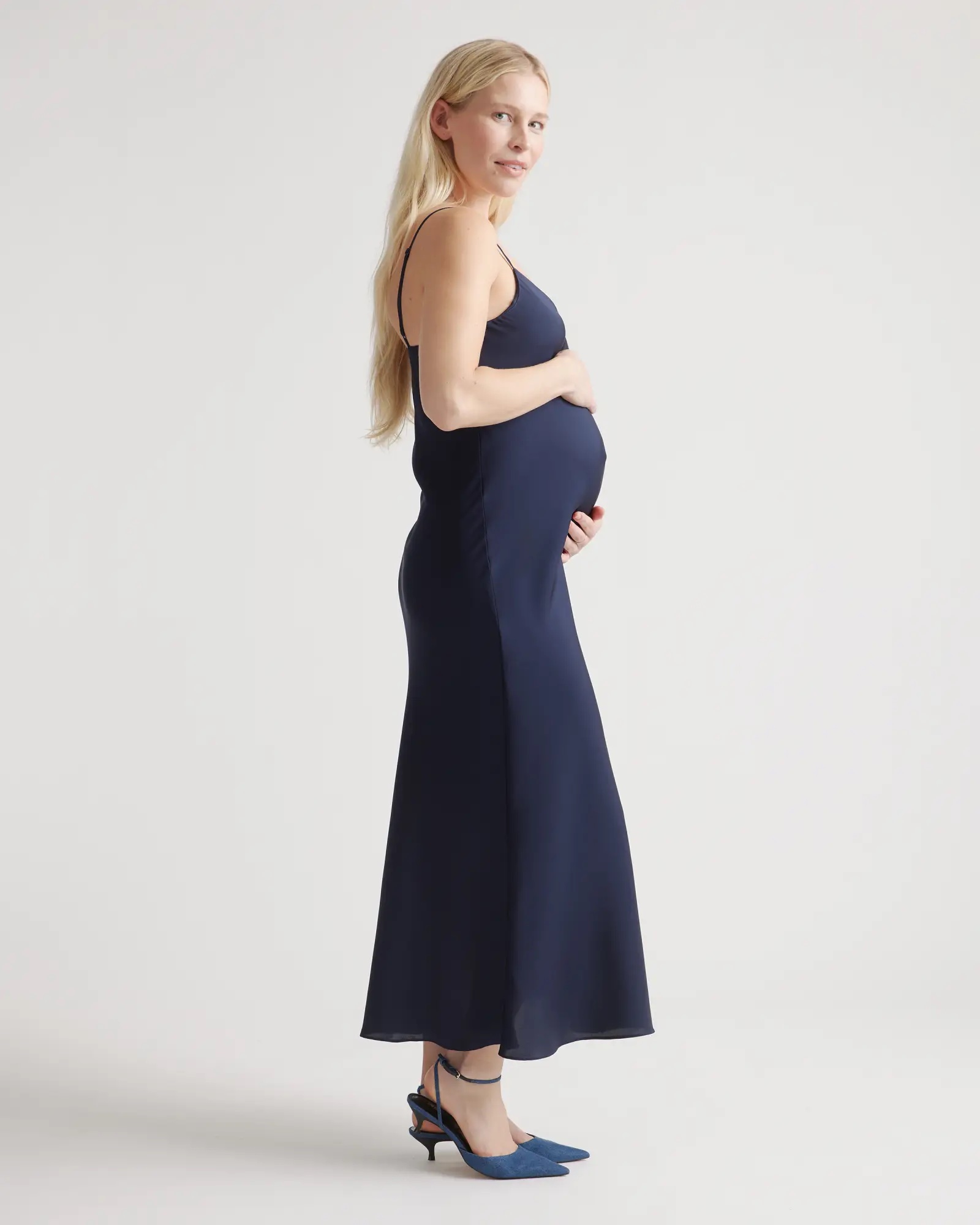 A model in a navy silk slip dress holds her baby bump. 