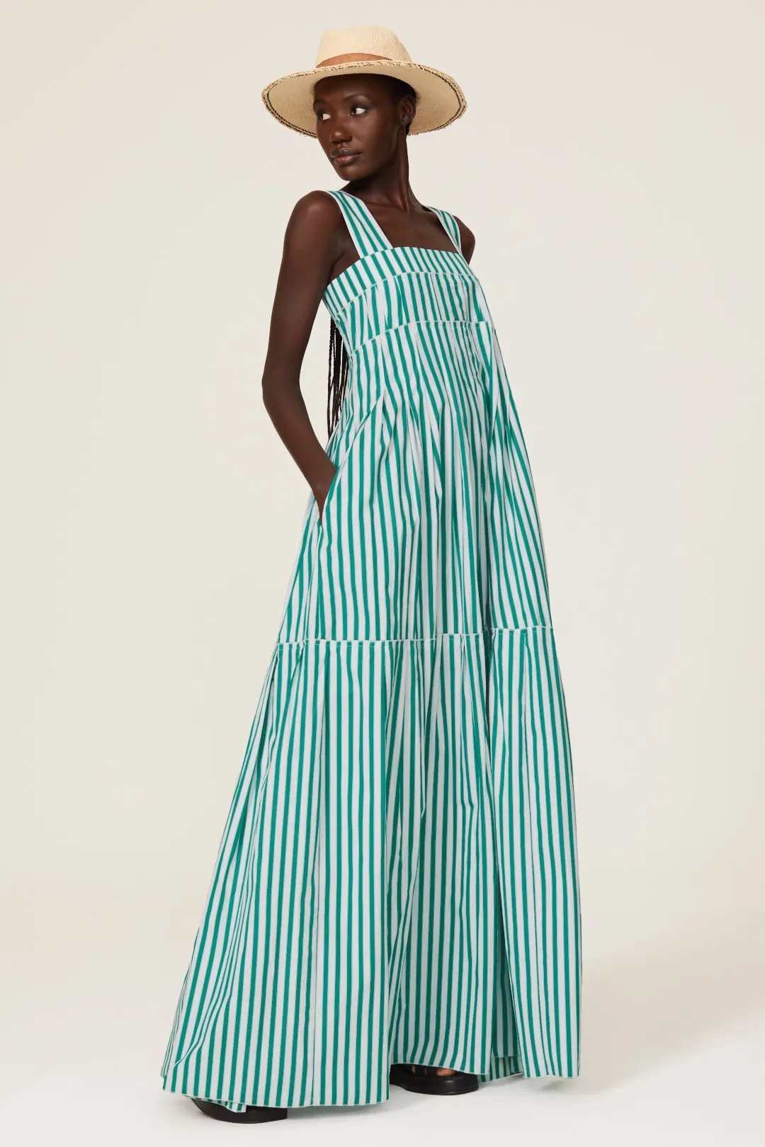 A model looks over her shoulder and has her hands in the pockets of a long green and white striped dress.