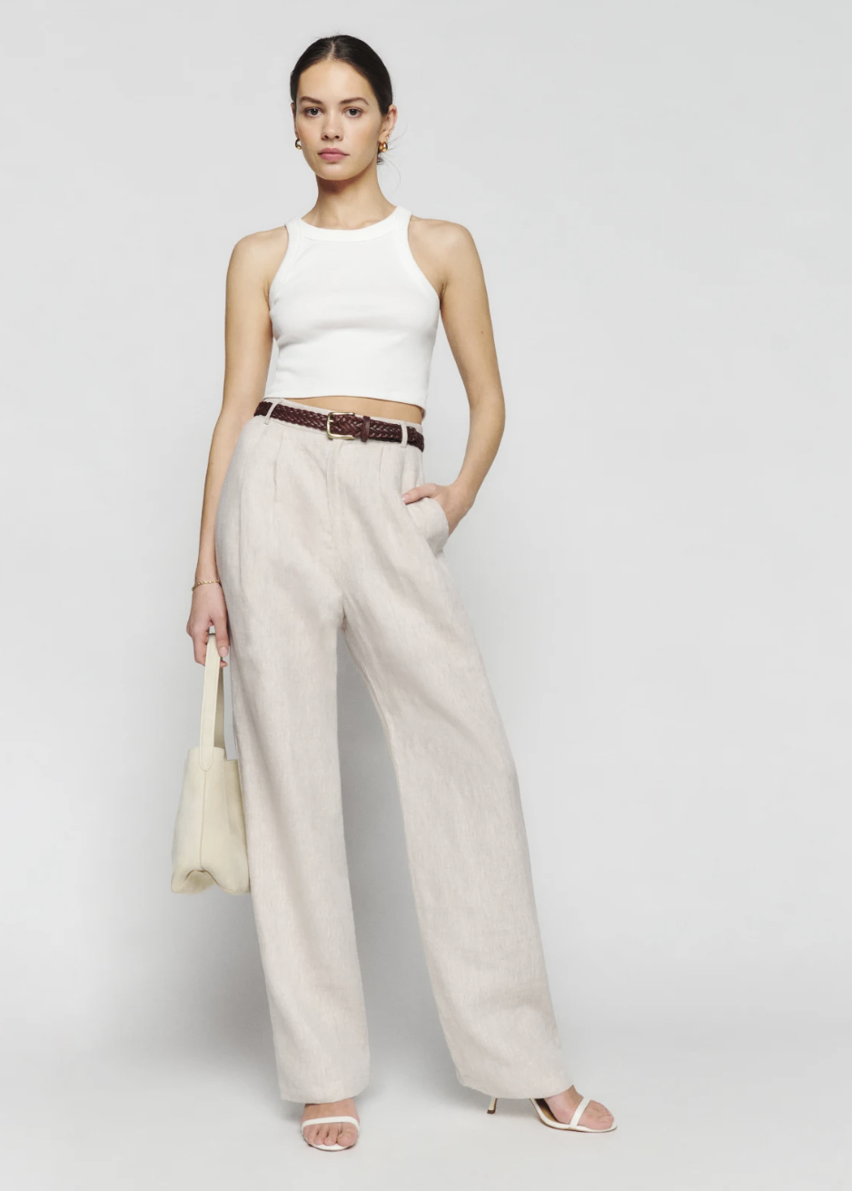 A model in a white tank and cream wide leg linen trousers.