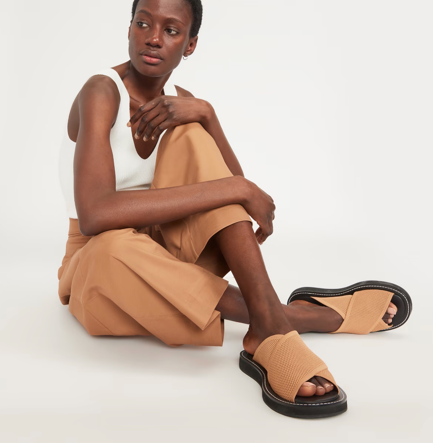 A model sits with her legs crossed, wearing Everlane sandals.