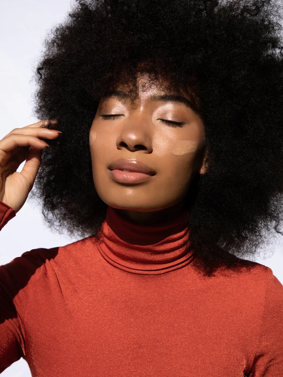 A Black model with natural hair closes her eyes and models sunscreen swatched on her cheeks