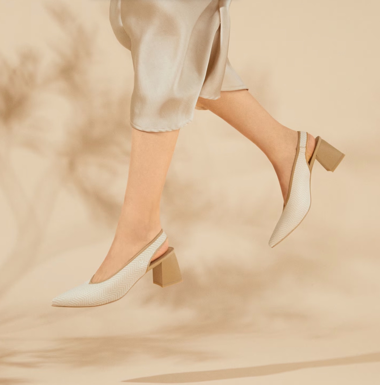A pair of feet wearing cream and tan block heeled sandals jump.