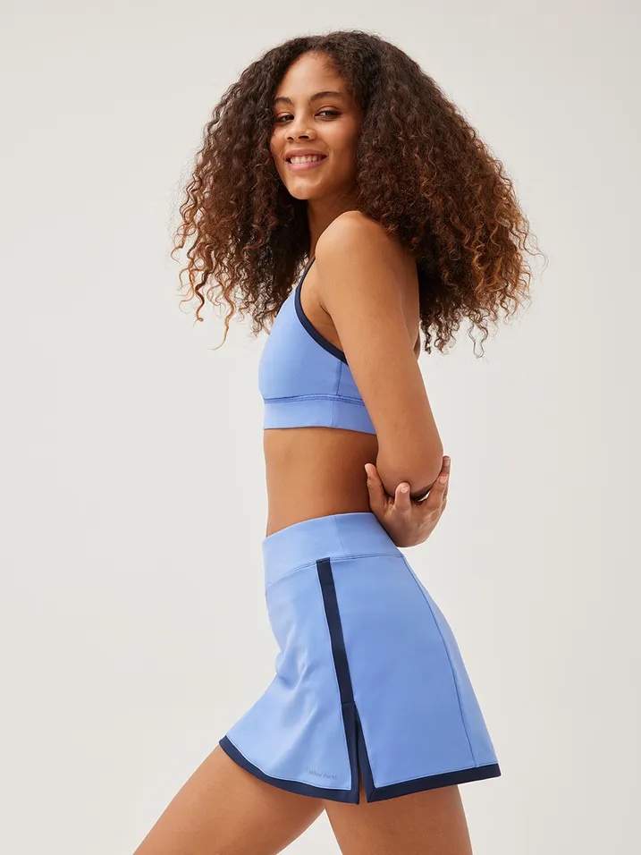 Model in matching cornflower blue skirt and sports bra with navy hem