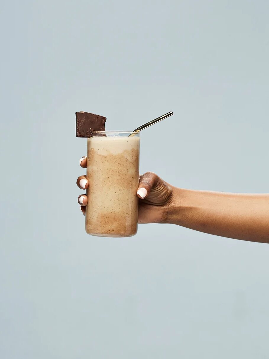 A hand holds a chocolate smoothie against a light blue background