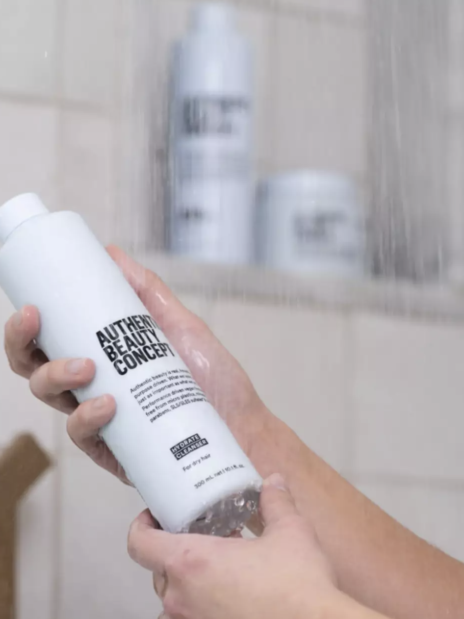 Hands hold the product out as though the model is reading the label in a shower.