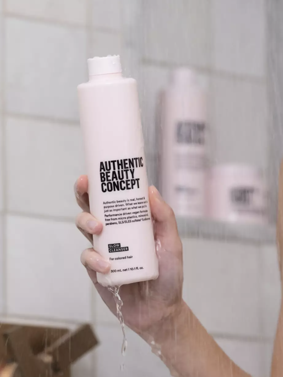 A hand holds up the product in a shower mist.