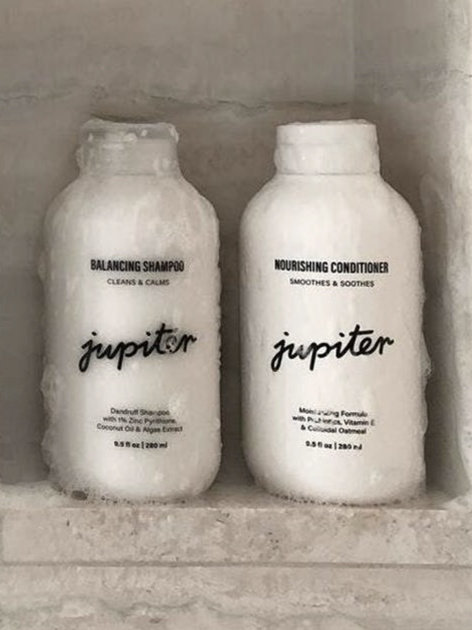 The shampoo and conditioner sit in a shower wall shelf covered in suds.