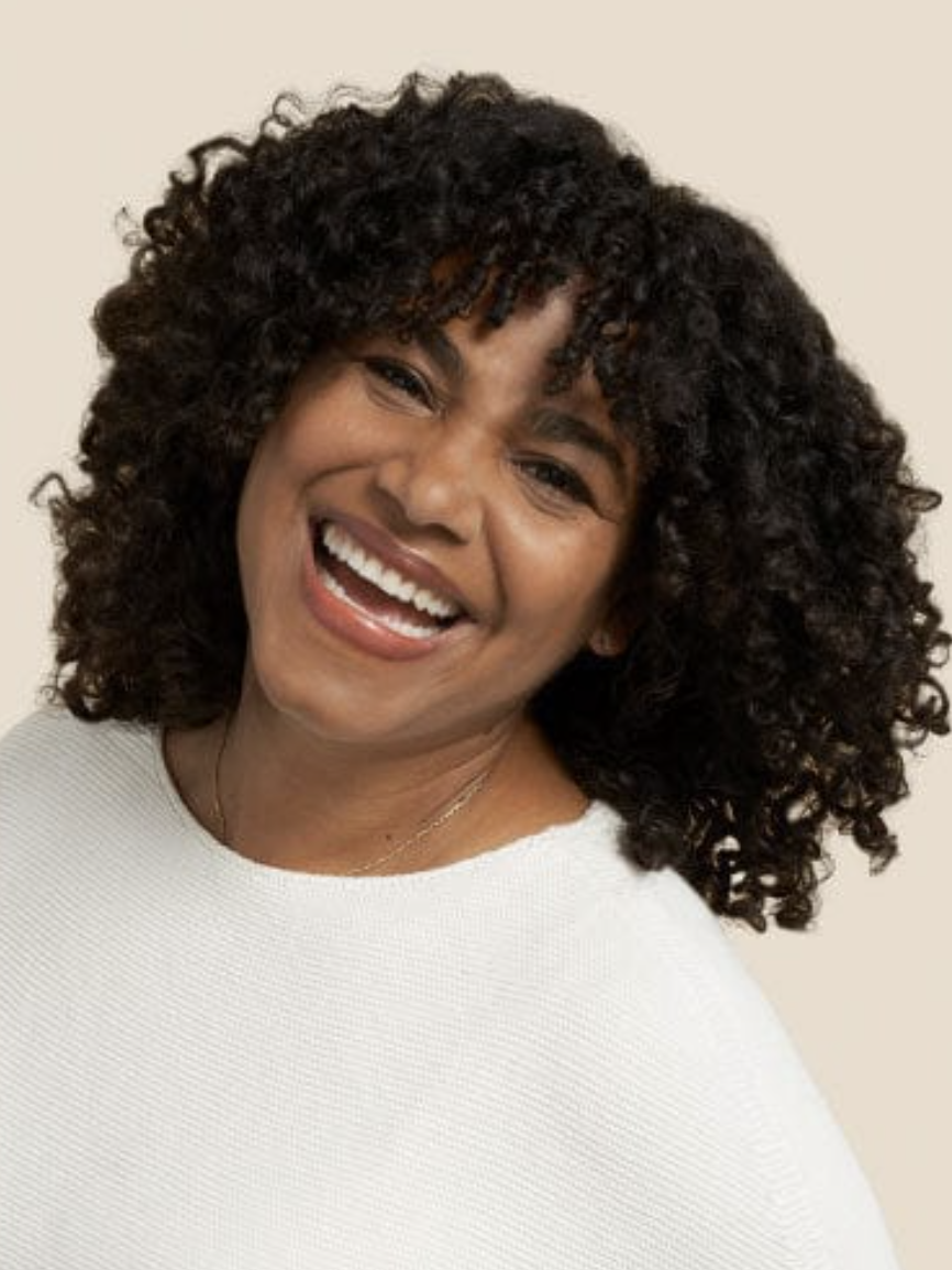 A Black model with curls smiles at the camera.