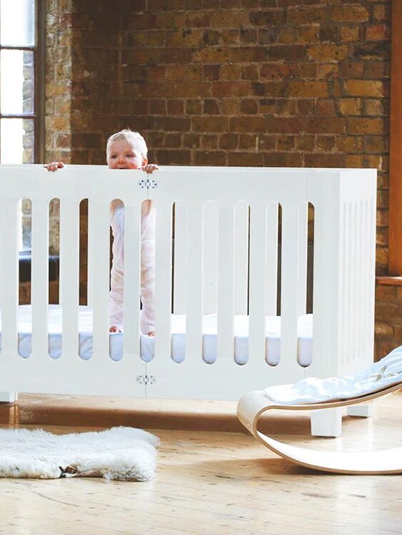 A baby stands in a white crib