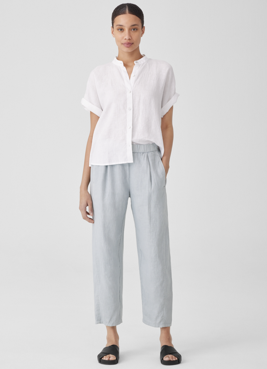 A model wearing pale blue pleated linen trousers and a white short sleeve button down.