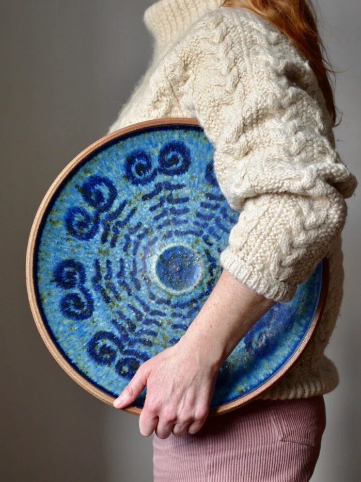 A woman holds a blue pottery disk