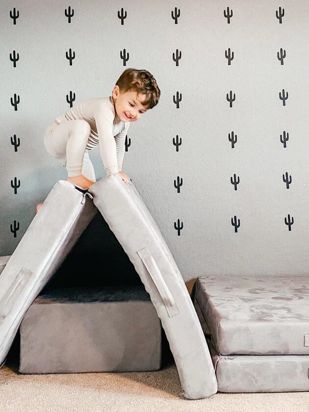 a boy climbs on a gray play cushion set into a triangle