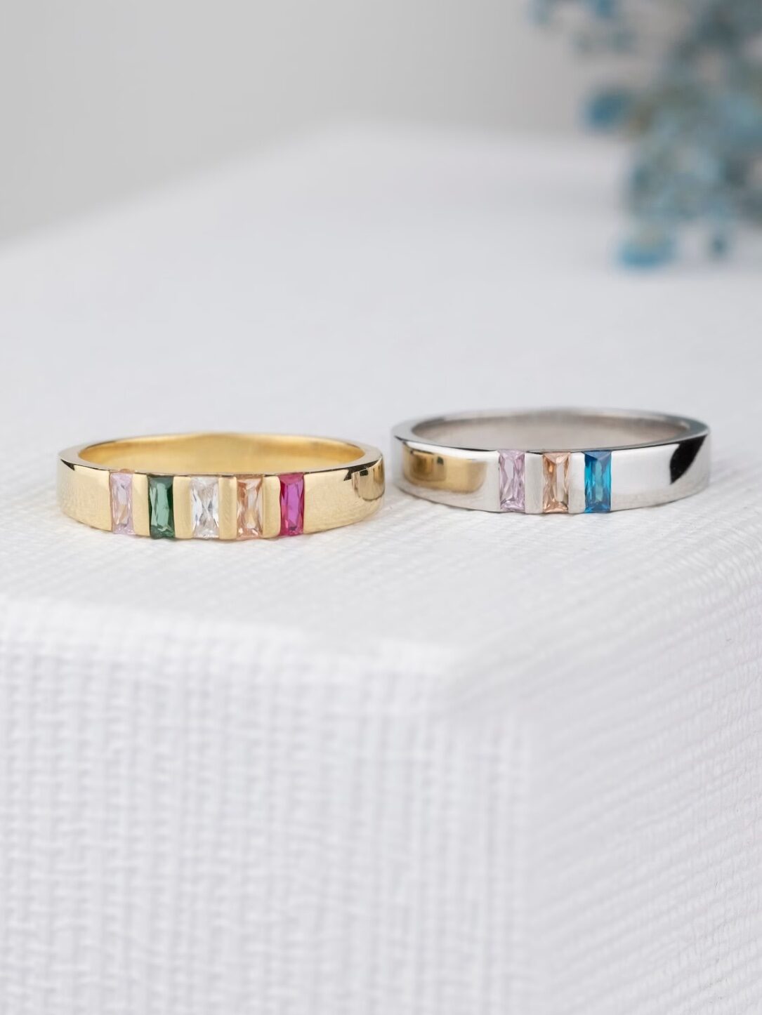 Gold and silver band rings with gemstones sit on a white surface