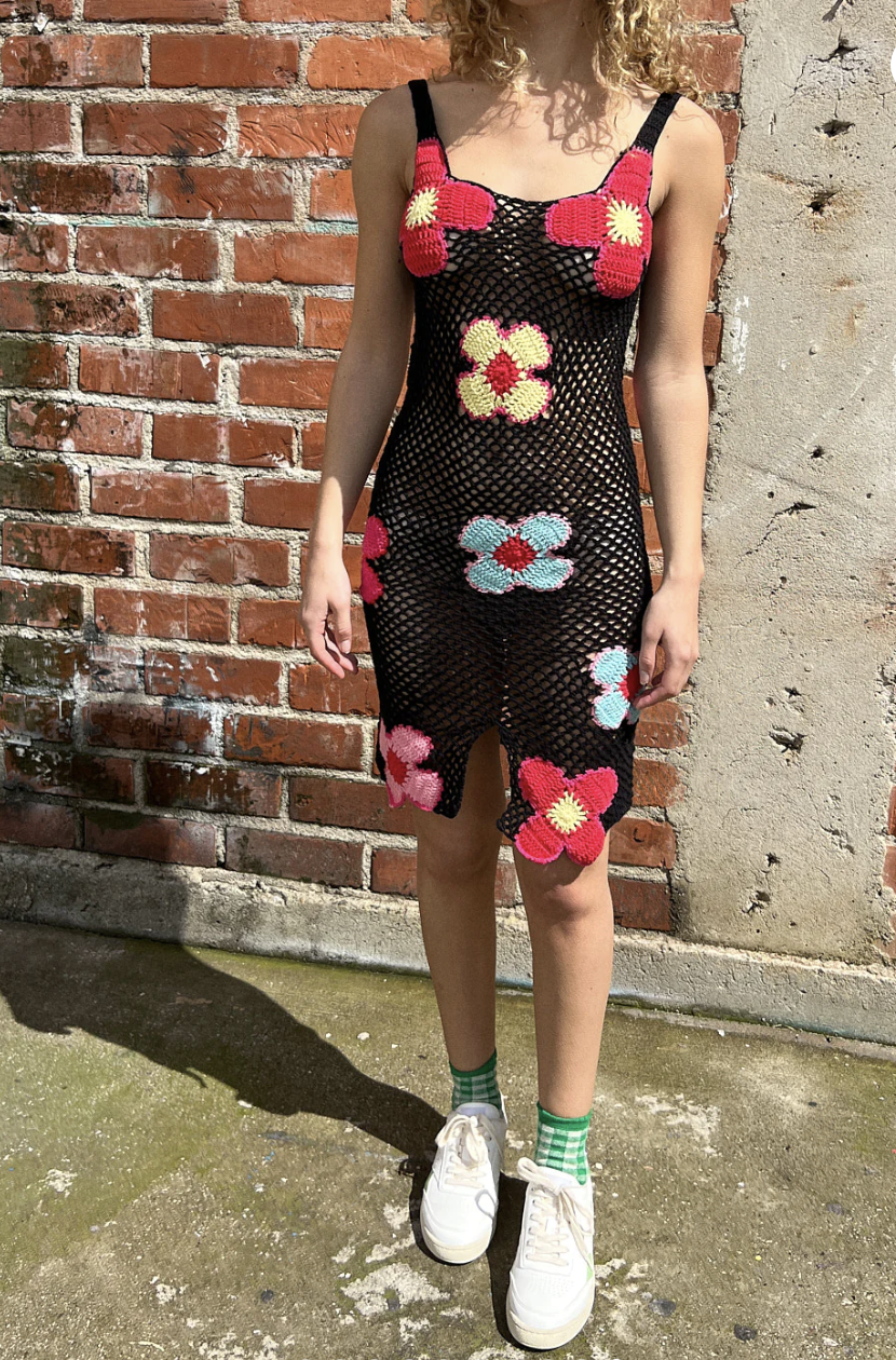 A woman models a black crochet dress with blue, pink, and red flowers