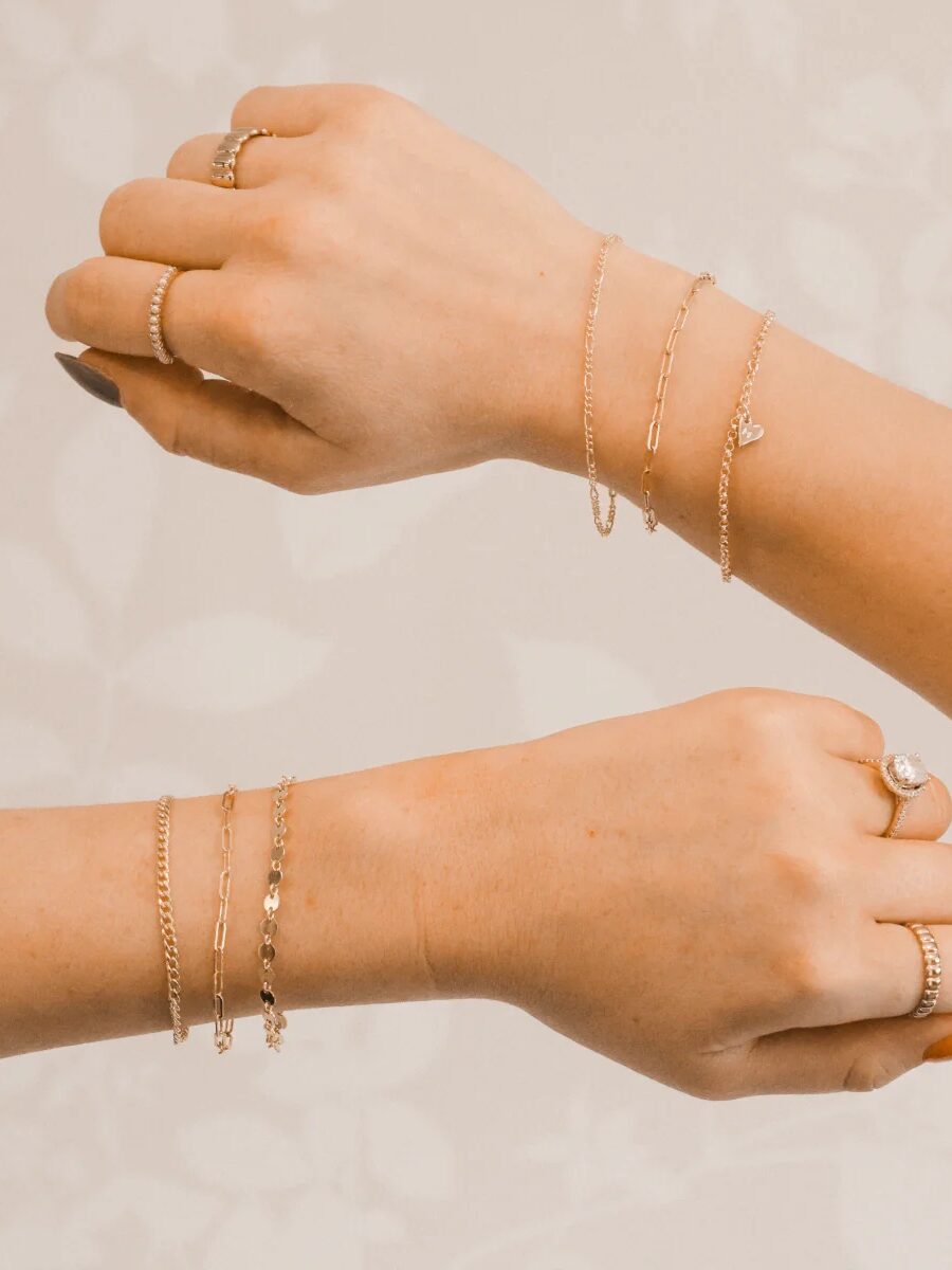 Two arms display a row of chain bracelets.