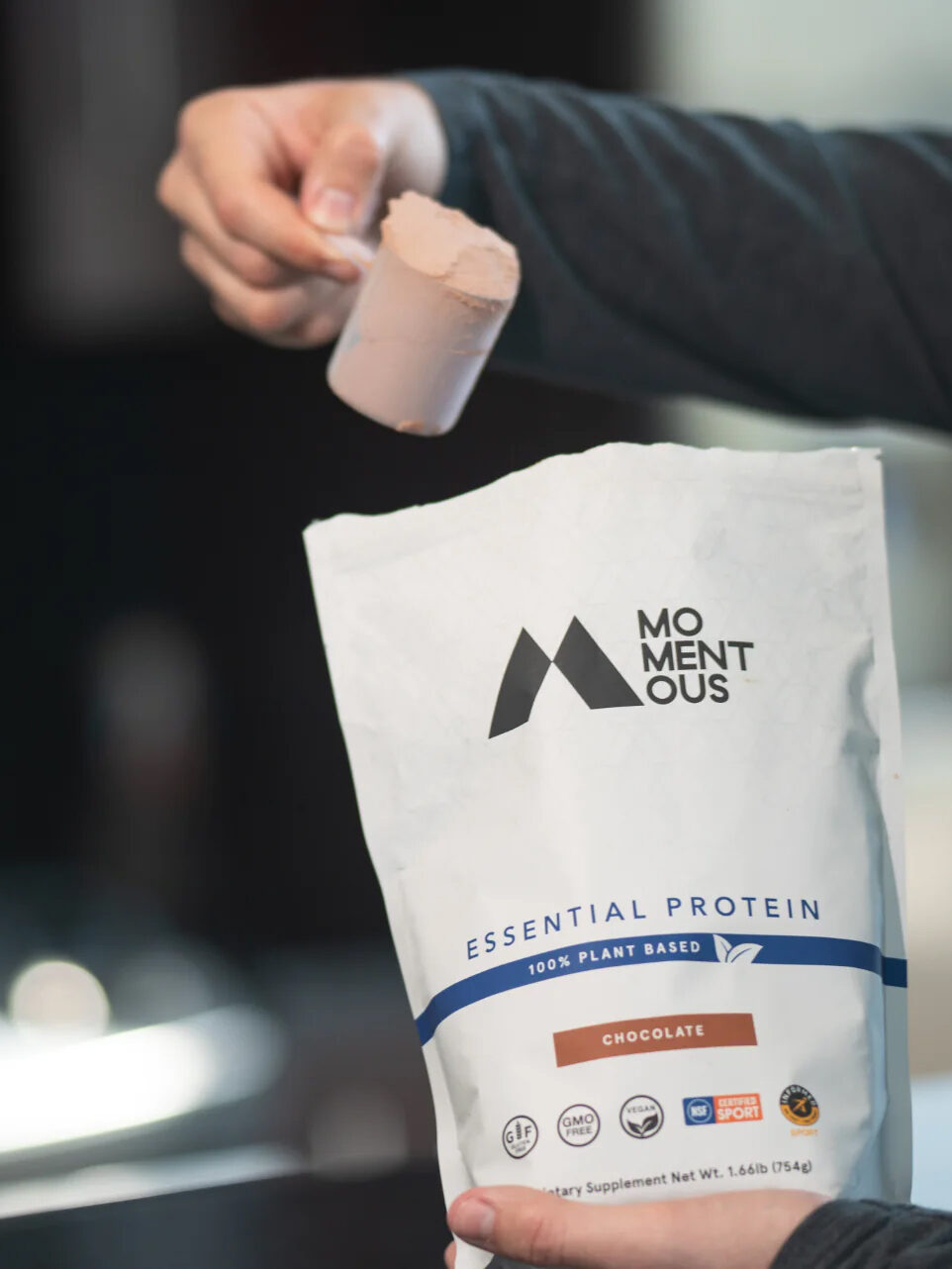 A hand scoops protein powder from a bag.