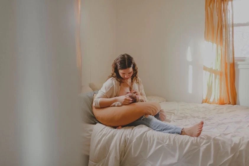 A woman nurses her baby on a peach colored pillow.