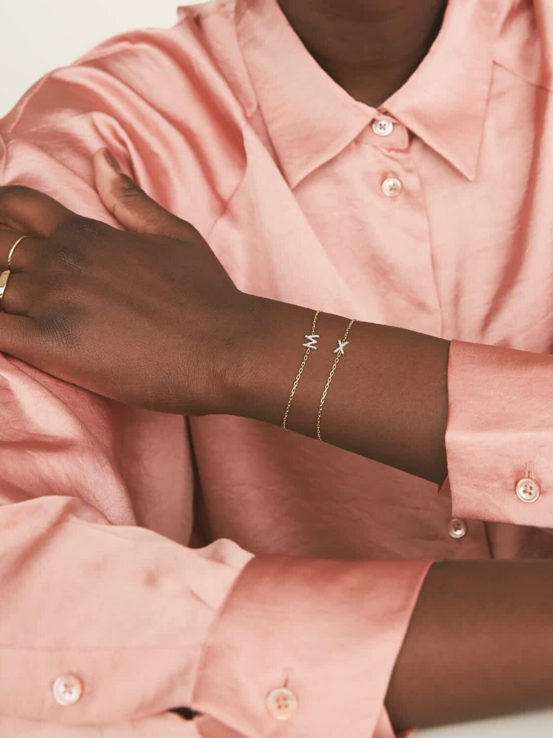 Initial charms on chain bracelets are displayed on a model's wrist