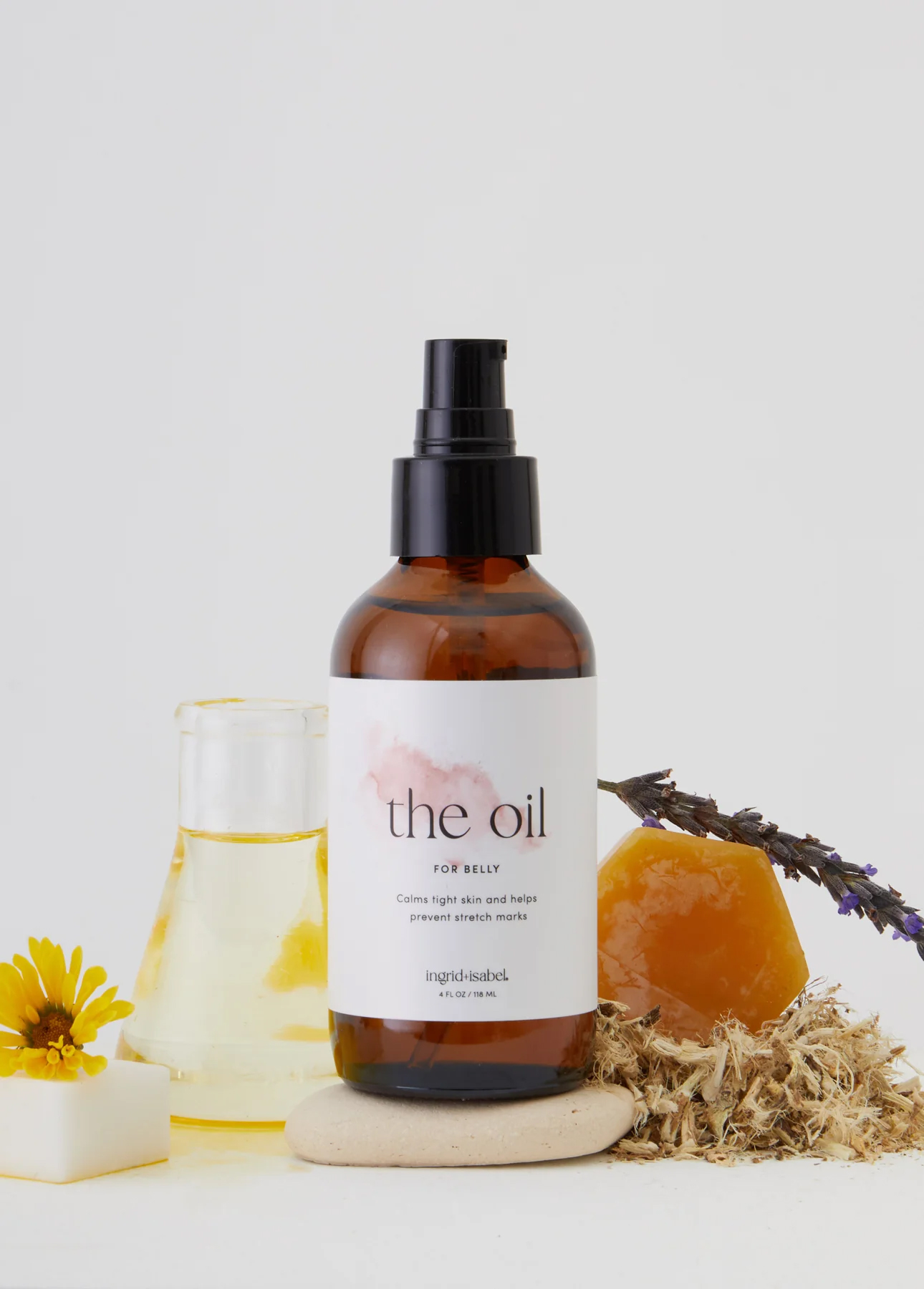 A bottle of body oil and several ingredients sitting around it. 